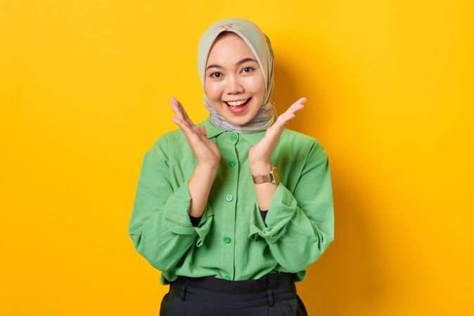Smiling Muslim woman in headscarf and green blouse with both hands surrounding her face