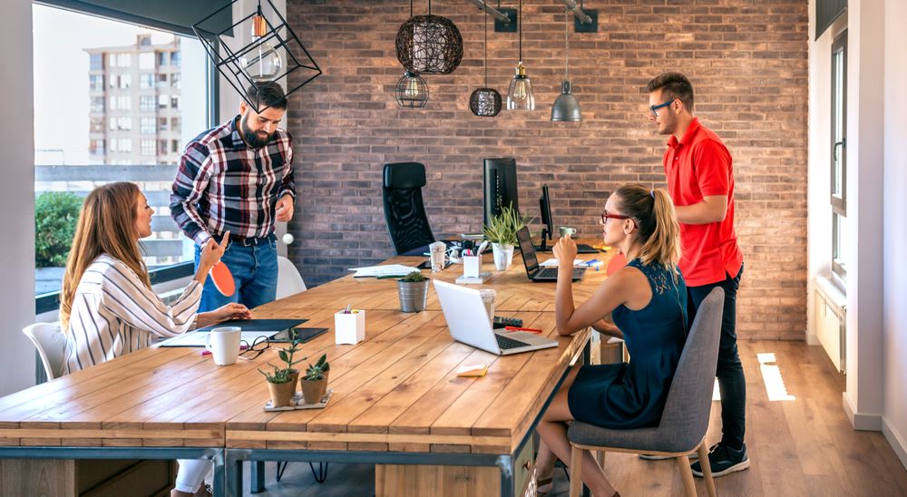 Colleagues talking in office while two of them having fun playing ping pong over coworking table
