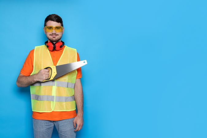 Engineer in glasses with saw in hands on blue background, space for text