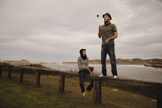 Man juggling balls on bench near woman with drum on shore