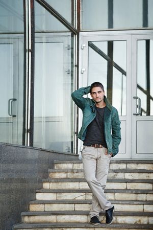 Male in green jacket standing running his hand through hair standing on steps to building