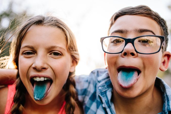 Happy teenage boy and girl having fun outdoors sticking out their tongues after candy