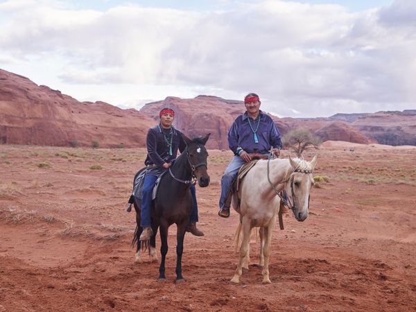 Two Navajo men sitting on horses in red sandy Arizona desert