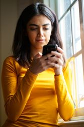 Woman texting on phone next to window
