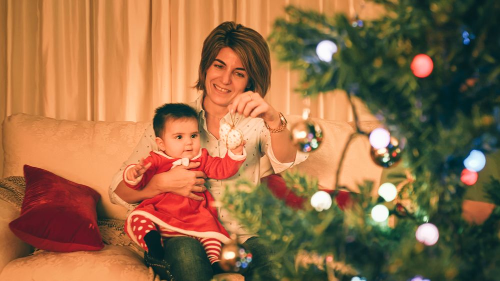 Mother playing with baby near Christmas tree
