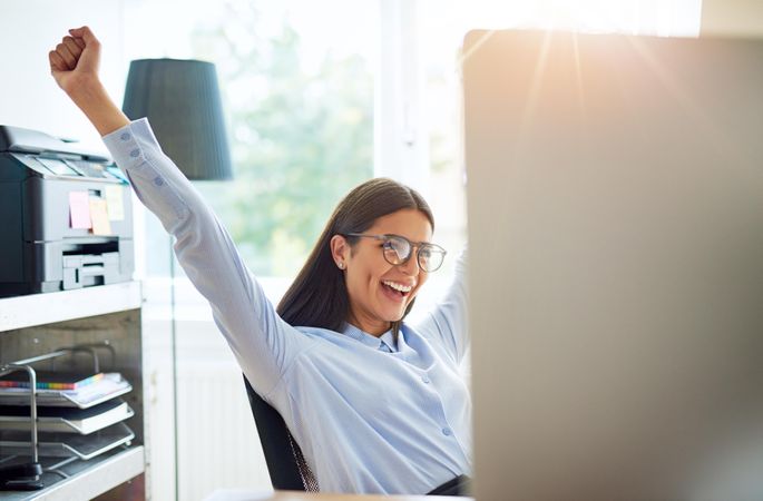 Happy woman raising hands in celebration in her bright home office