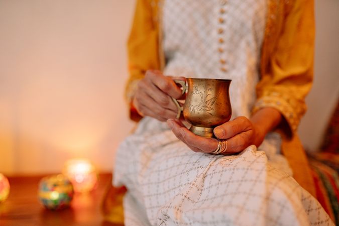 Cropped image of woman holding a cupper mug sitting beside Diwali's candles