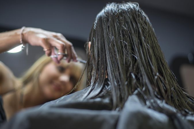 Brunette woman with wet hair being cut in salon