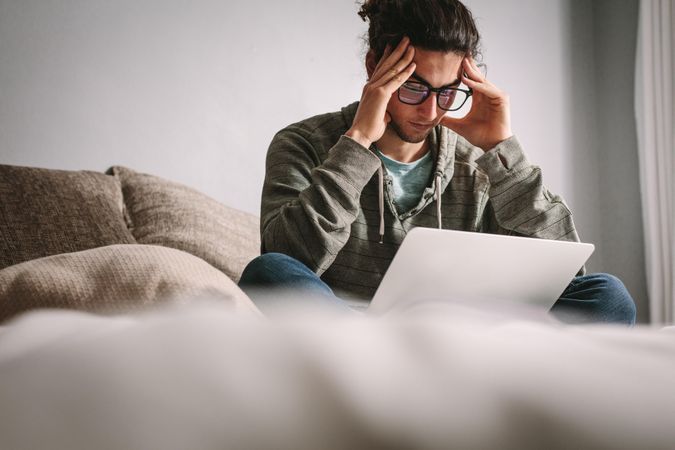 Stressed student studying at home with laptop on couch
