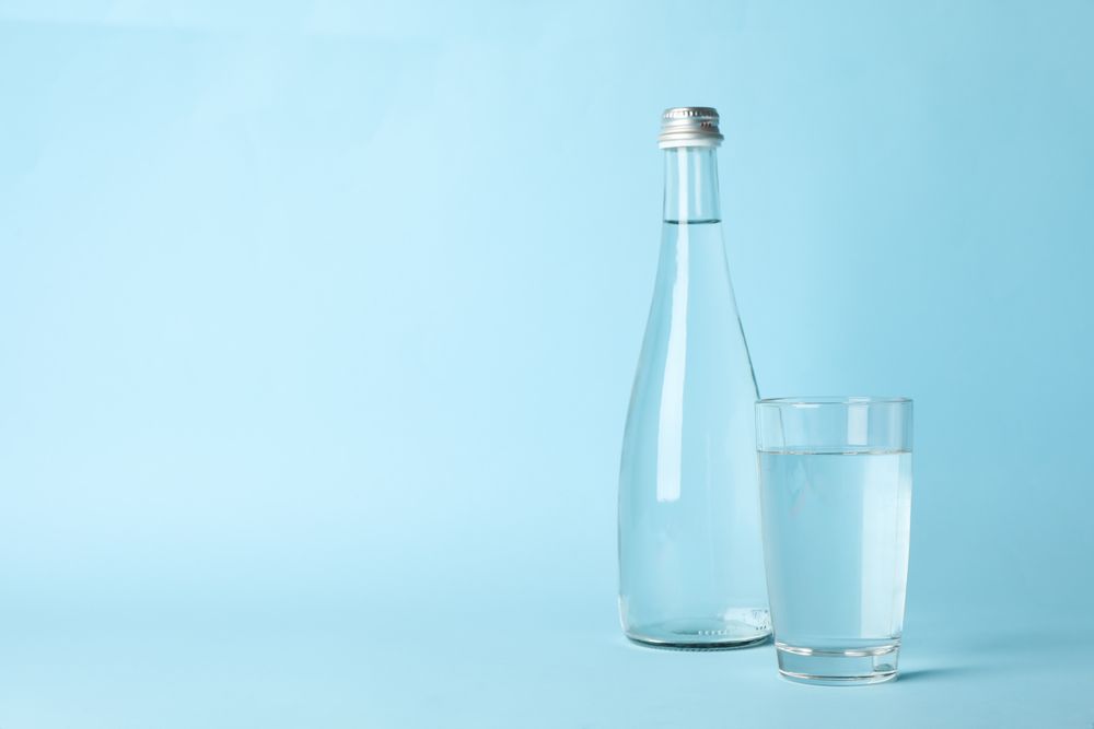 Water bottle with glass full of water in light blue space
