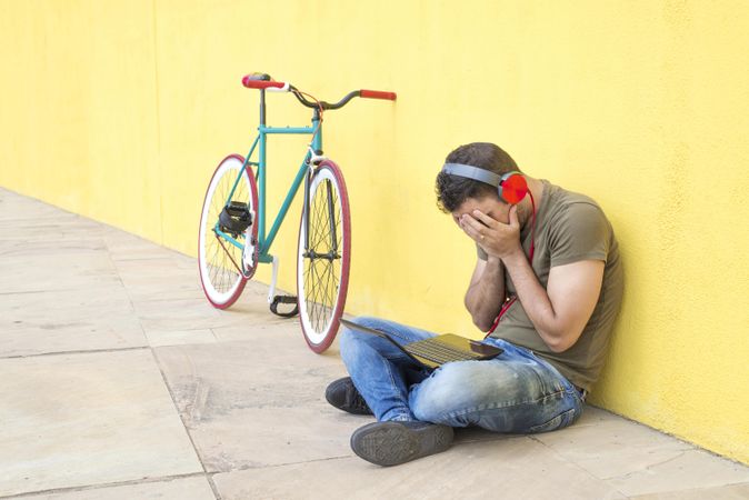 Defeated male with red headphones sitting outside concentrating on laptop