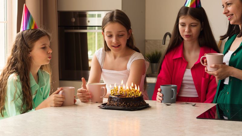 Girl blowing out candles on birthday cake surrounded by family.