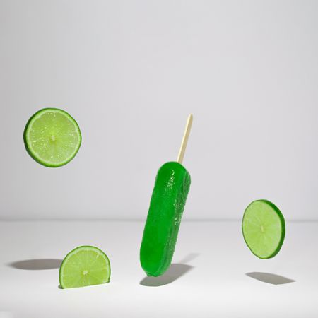 Green ice pops  and slices of limes suspended with shadow in grey room