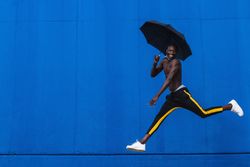 Cheerful Black man with umbrella jumping on street