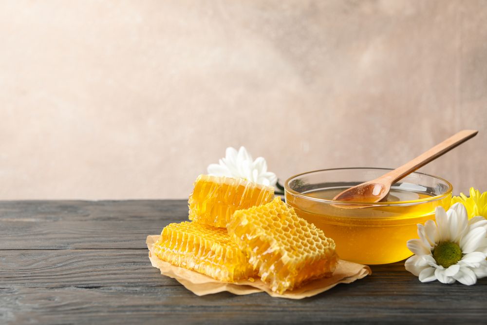 Bowl with honey, honeycombs and flowers on wooden background, copy space