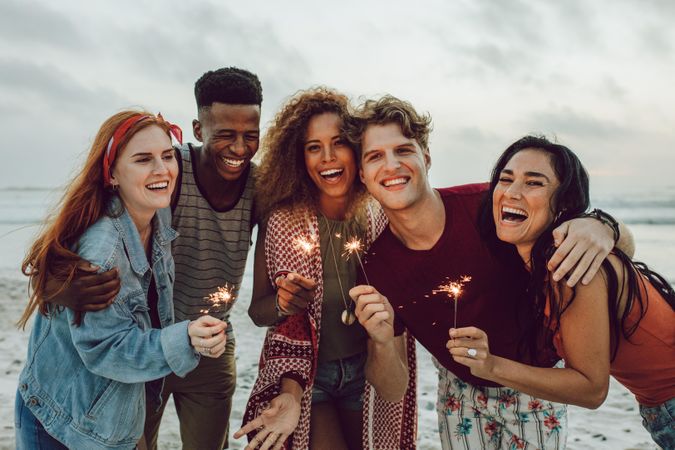 Group of friends hugging and lighting sparklers on the beach