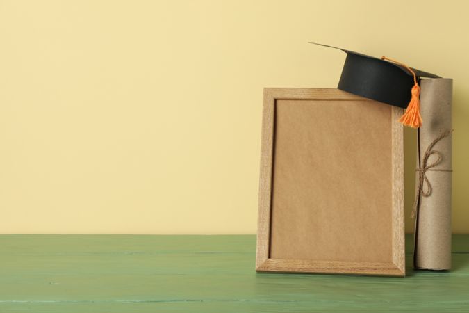 Frame and graduate hat with books on table.