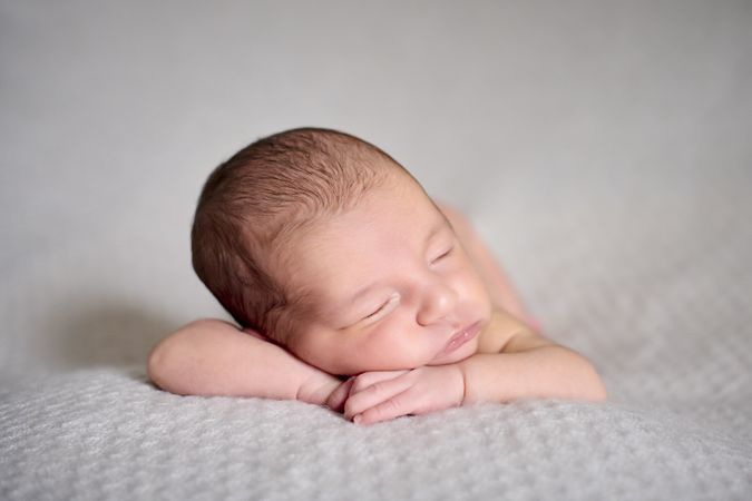 A naked newborn sleeping on her hands on top of a gray blanket