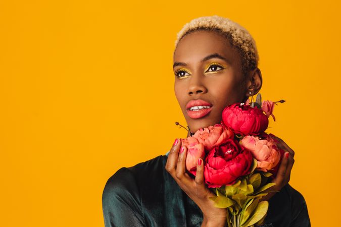 Black woman with short blonde hair holding bouquet of large red flowers