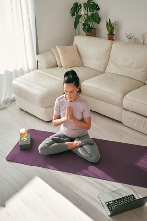 Hispanic woman meditating with namaste hands near beer and laptop