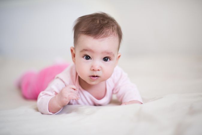 Baby in pink pant and shirt crawling on textile