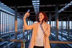 Smiling young woman taking selfie at station