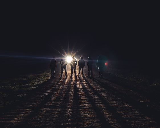 Group of people standing in the dark in front of car light