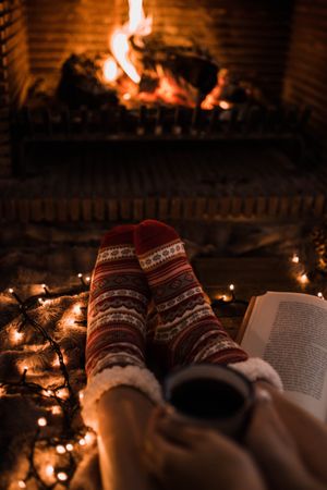 Faceless woman sitting by fireplace and holding mug