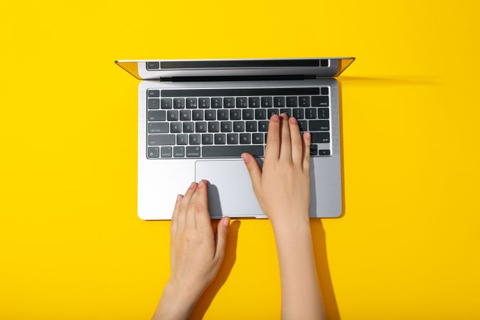 Top view of person using laptop on yellow desk