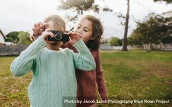Two little girls taking photographs using camera at the playground 4OxmRb