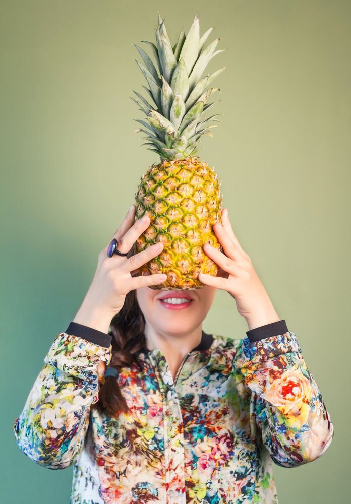 Woman holding pineapple in front of face