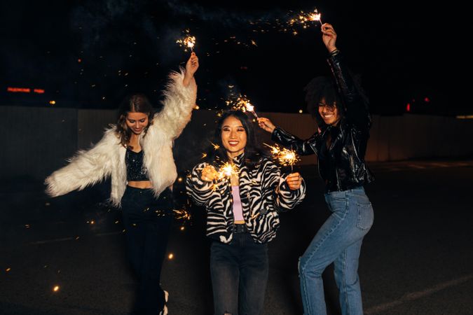 Three happy women celebrating at night with sparklers
