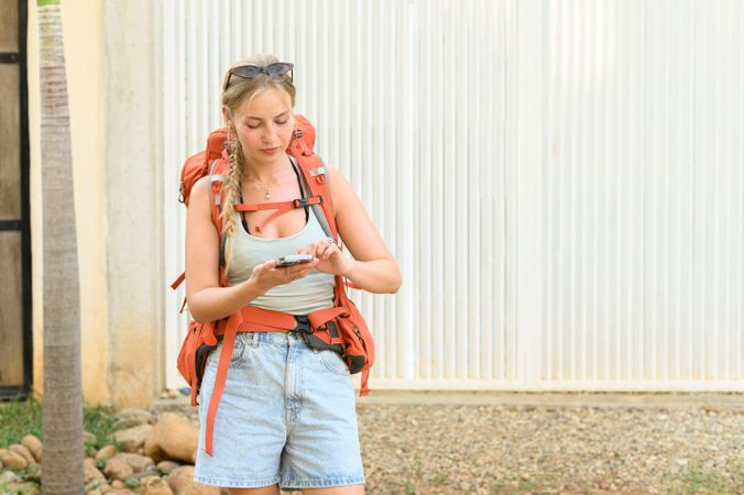 Young traveling woman checking smartphone on street against white background