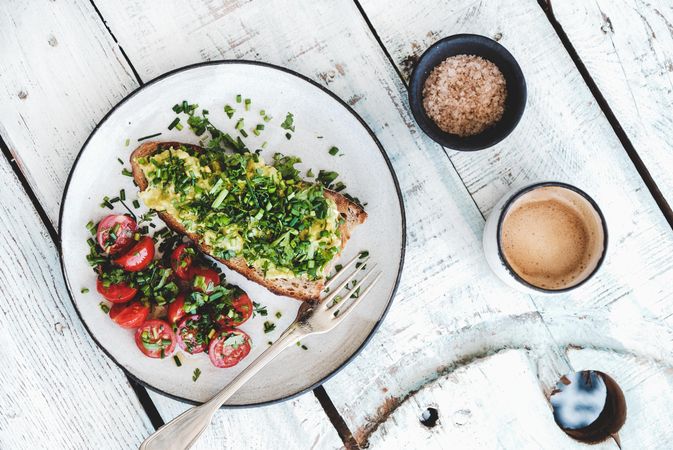 Avocado toast on sourdough bread, cherry tomatoes, coffee and bowl, on light background, top view