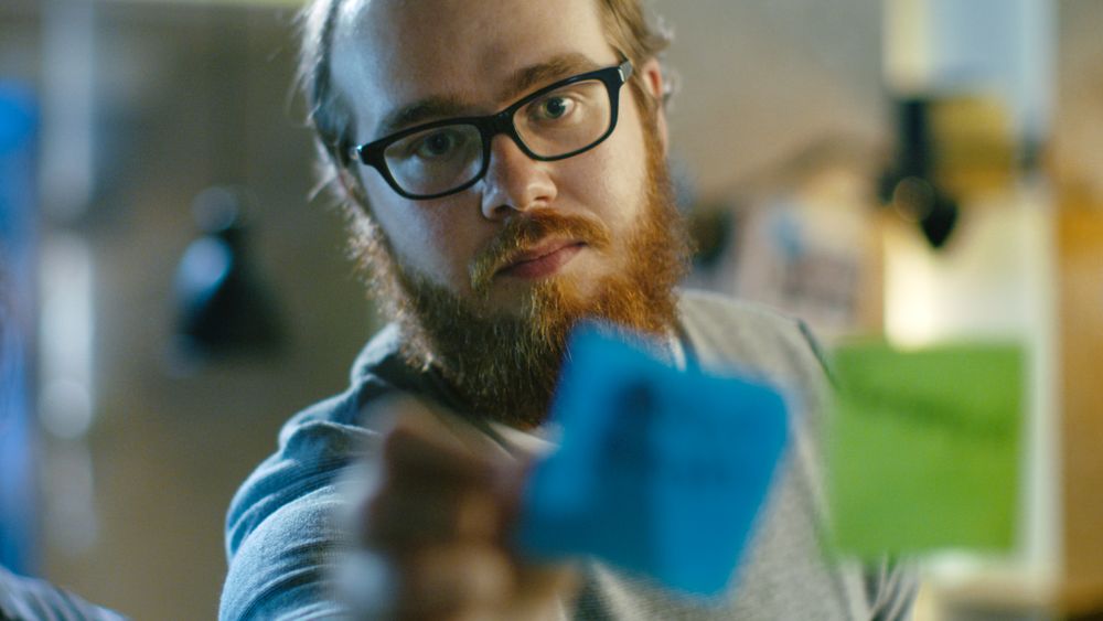 Male Designer Plan His Next Project on a Glass Wall with Sticky Notes Outline.