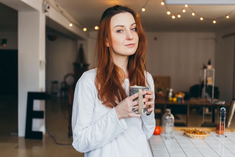 Woman looks up while holding mug of a warm drink in her apartment