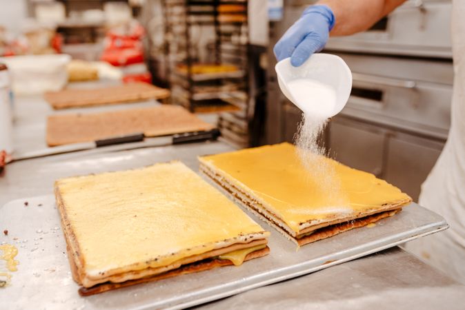 Crop confectioner spilling sugar on cake