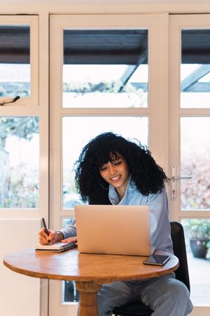 Black woman working on laptop and writing notes