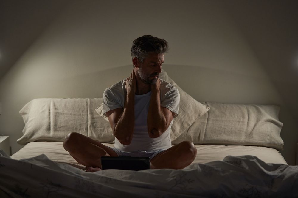 Exhausted mature ethnic man resting after working on tablet in bed