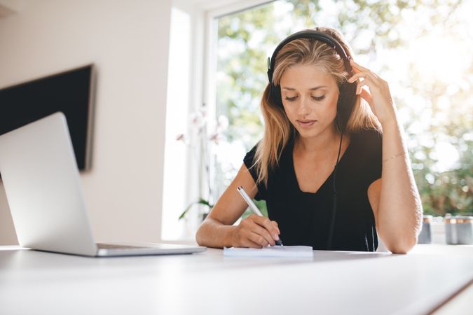 Woman studying in kitchen with laptop and headphones