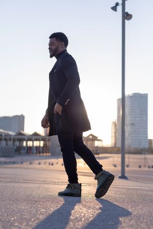 Black man walking outdoors with sunsetting behind him