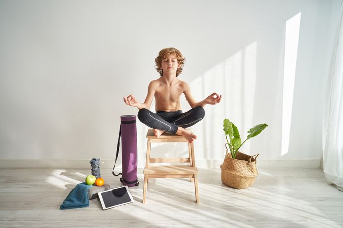 Concentrated boy meditating in Lotus pose on wooden stool