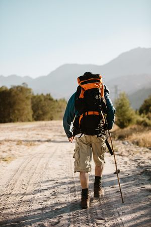 Rear view of man with backpack walking over a mountain trail