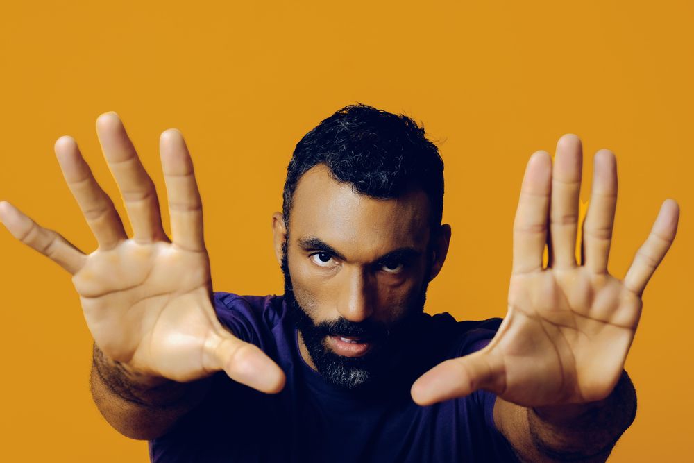 Serious Black man in yellow studio with hands outstretched towards the camera