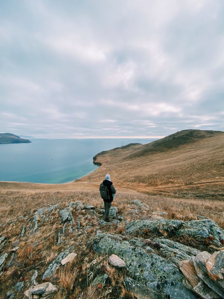 Back view of person with backpack standing on rock formation near seashore