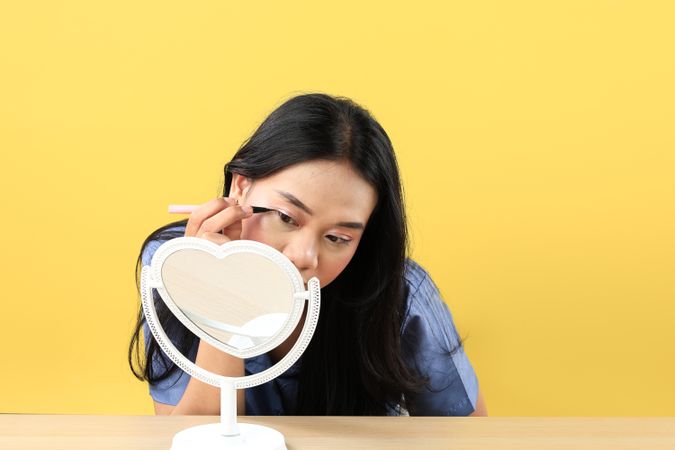 Young Asian Woman Applying Make-up to Her Face, using Eyeliner for Eyes and Looking at the Mini Standing Mirror