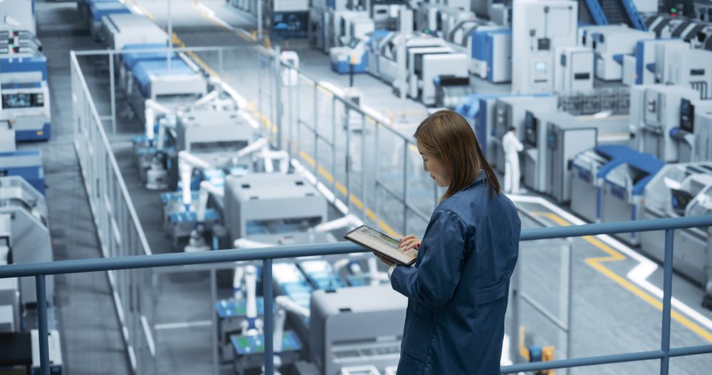 Portrait of a Japanese Engineer Using Tablet Computer and Looking Around a Factory Facility with Equipment Producing Modern Electronic Components for Different Industries