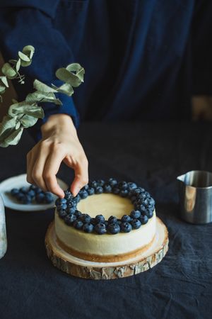 Person adding fresh organic blueberries to top of cheesecake