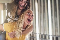 Playful blonde woman carrying friend on her back