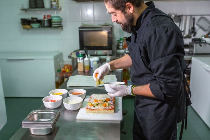 Portrait of male chef adding fresh healthy ingredients to vegetarian focaccia in restaurant kitchen
